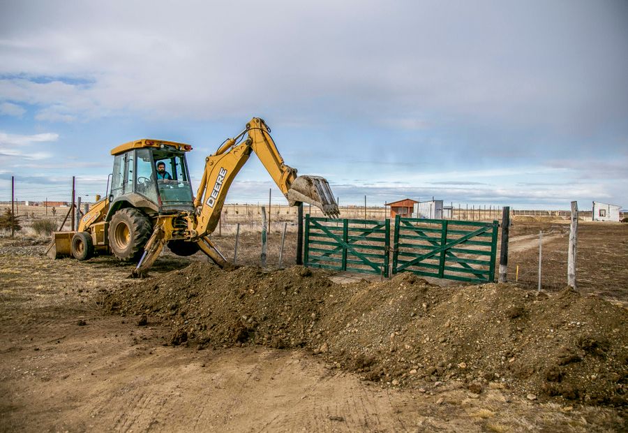 Backhoe opening the ground at a rural field gate to swap a culvert pipe